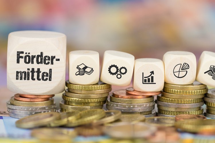 Euer Studium Sieben Würfel mit der Aufschrift Fördermittel sowie Grafiken, die Geld, Zahnräder, Tabellen zeigen, liegen aufgereiht auf Euromünzen.