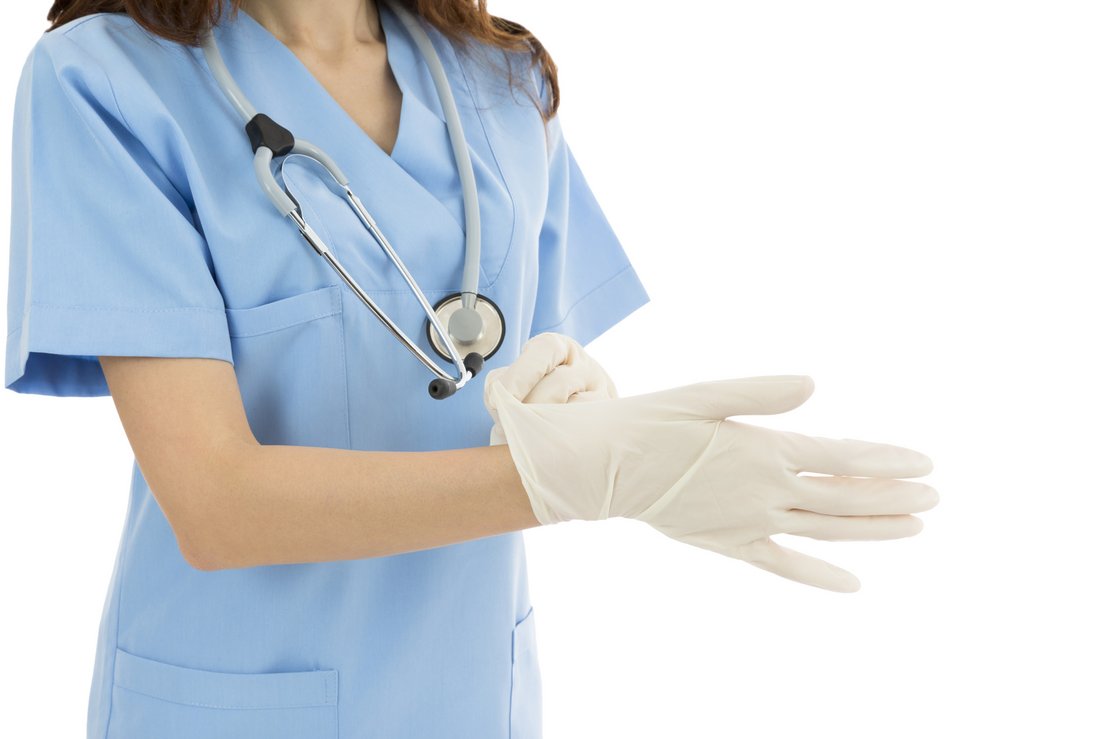 Eine Ärztin in blauem Kasak mit Stethoskop um den Hals, zieht sich Handschuhe an.