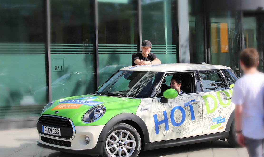 Mini Cooper im Kampagnendesign Sei Ärztin Praxis Leb Hessen. Frau sitzt im Auto. Man lehnt sich auf das Auto