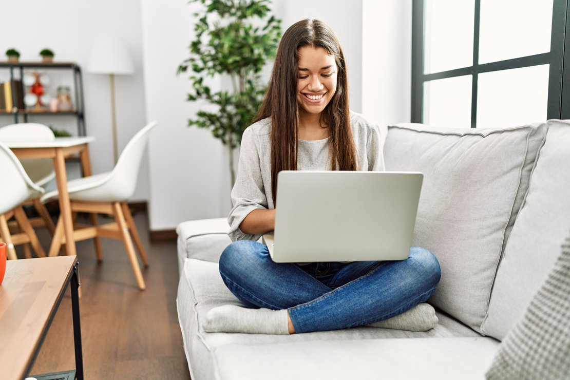 Junge Dame im Schneidersitz auf dem Sofa mit einem Laptop auf dem Schoß